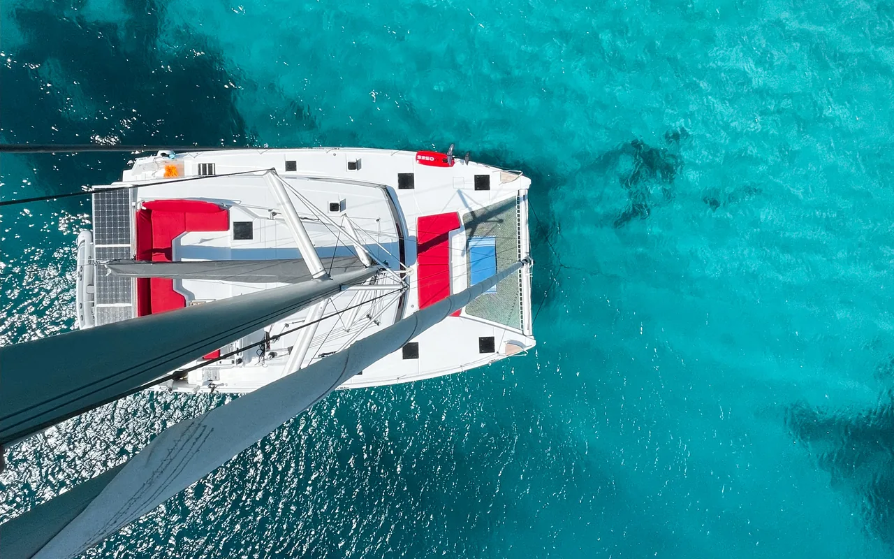 Aerial drone shot of the Makani catamaran anchored in turquoise Cyclades water.