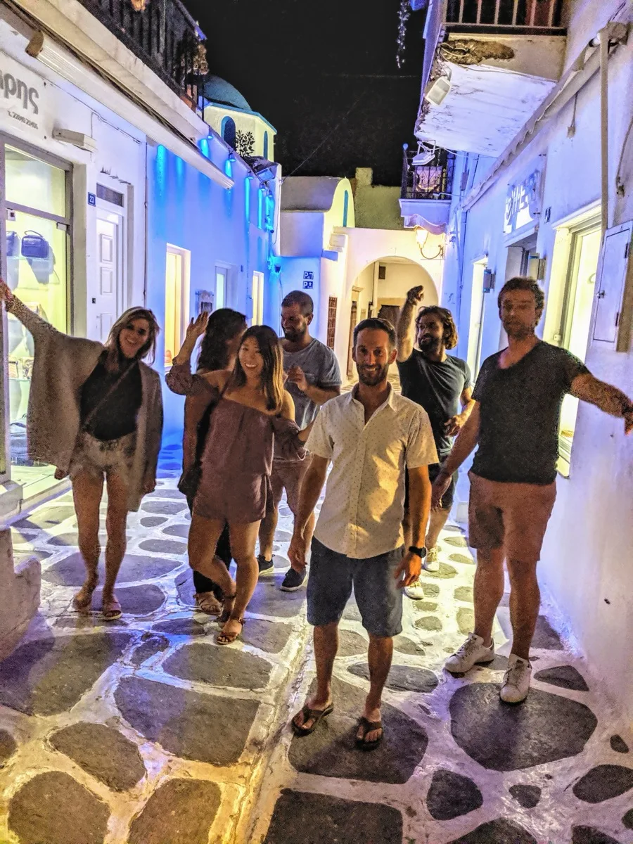 Guests exploring the marble-paved alleys of a Cyclades island town at night.