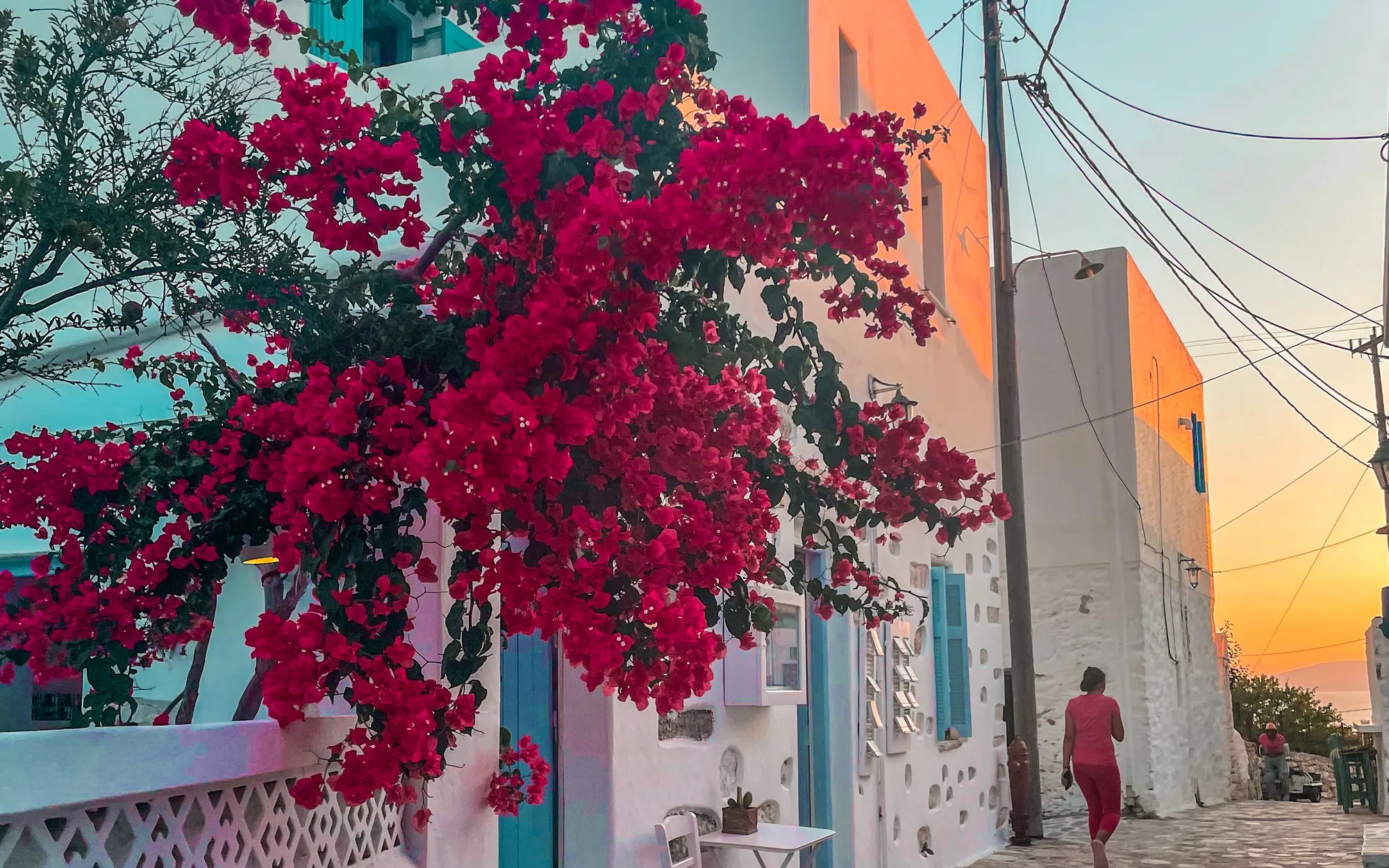 A whitewashed Cycladic lane under pink bougainvillea at sunset.